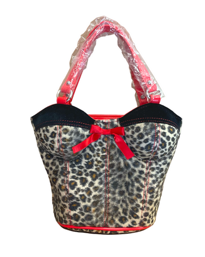 A leopard print bag with black trim, a red bow, and bright red handles still wrapped in protective plastic, set against a plain brown background.