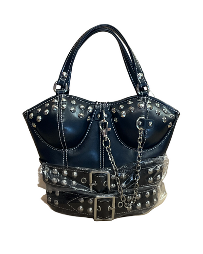 A structured black faux-leather handbag with silver studs, double top handles, a chain strap, and a wide studded belt detail wrapped in protective plastic, set against a plain brown paper background.